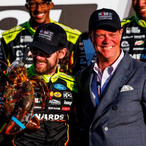 2023 NASCAR Cup Series champion Ryan Blaney (left), driver of the No. 12 Team Penske Ford, looks affectionately at Loudon the Lobster in victory lane at New Hampshire Motor Speedway on Sept. 21, 2025 with NHMS Executive Vice President and General Manager David McGrath (right).