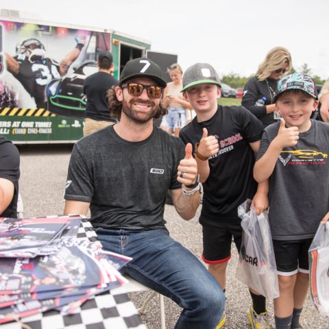 NASCAR Cup Series driver Corey LaJoie gives a thumbs up with two young fans at New Hampshire Motor Speedway in 2022.