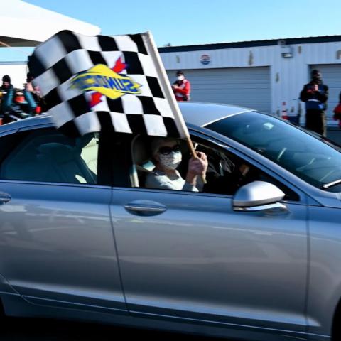 A Granite State couple waves the checkered flag after receiving the last COVID-19 vaccine shots at New Hampshire Motor Speedway’s vaccine super site on March 8.