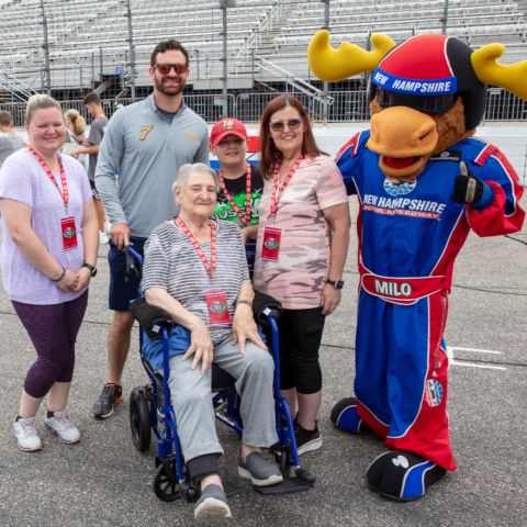 NASCAR Cup Series driver Corey LaJoie (second from left) and New Hampshire Motor Speedway (NHMS) mascot Milo the Moose (far right) posed for a picture with race fans at NHMS during the annual Track Walk event to benefit the New Hampshire Chapter of Speedway Children’s Charities on July 15.