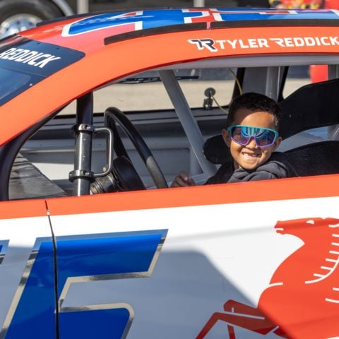 A young race fan gets behind the wheel of NASCAR Cup Series driver Tyler Reddick’s No. 45 23XI Toyota show car in the Fan Zone at New Hampshire Motor Speedway on Sept. 21, 2025. 